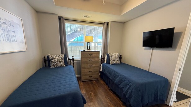 Un dormitorio con dos camas, un aparador, un televisor y una ventana con persianas.