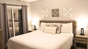 Un dormitorio con una cama grande, un ventanal corredero y tres adornos colgados en la pared.