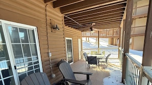 Varanda coberta com piso de madeira, duas cadeiras Adirondack, uma mesa e vista para uma paisagem nevada.