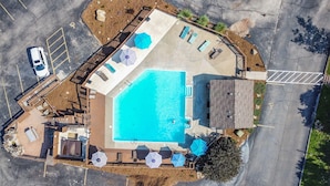 Vista aérea de uma área de piscina com deck, cadeiras de descanso e guarda-sóis.