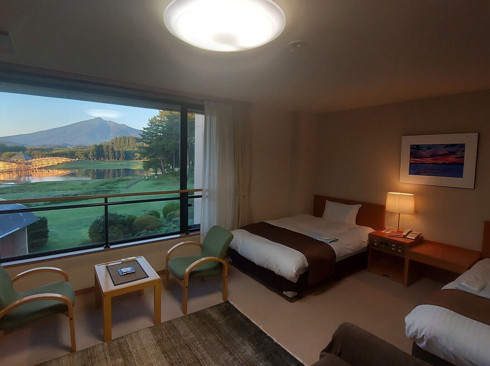 Habitació d'hotel amb llit, escriptori, dues cadires, taula de nit amb làmpada i una finestra gran que dona a un camp de golf i una muntanya.