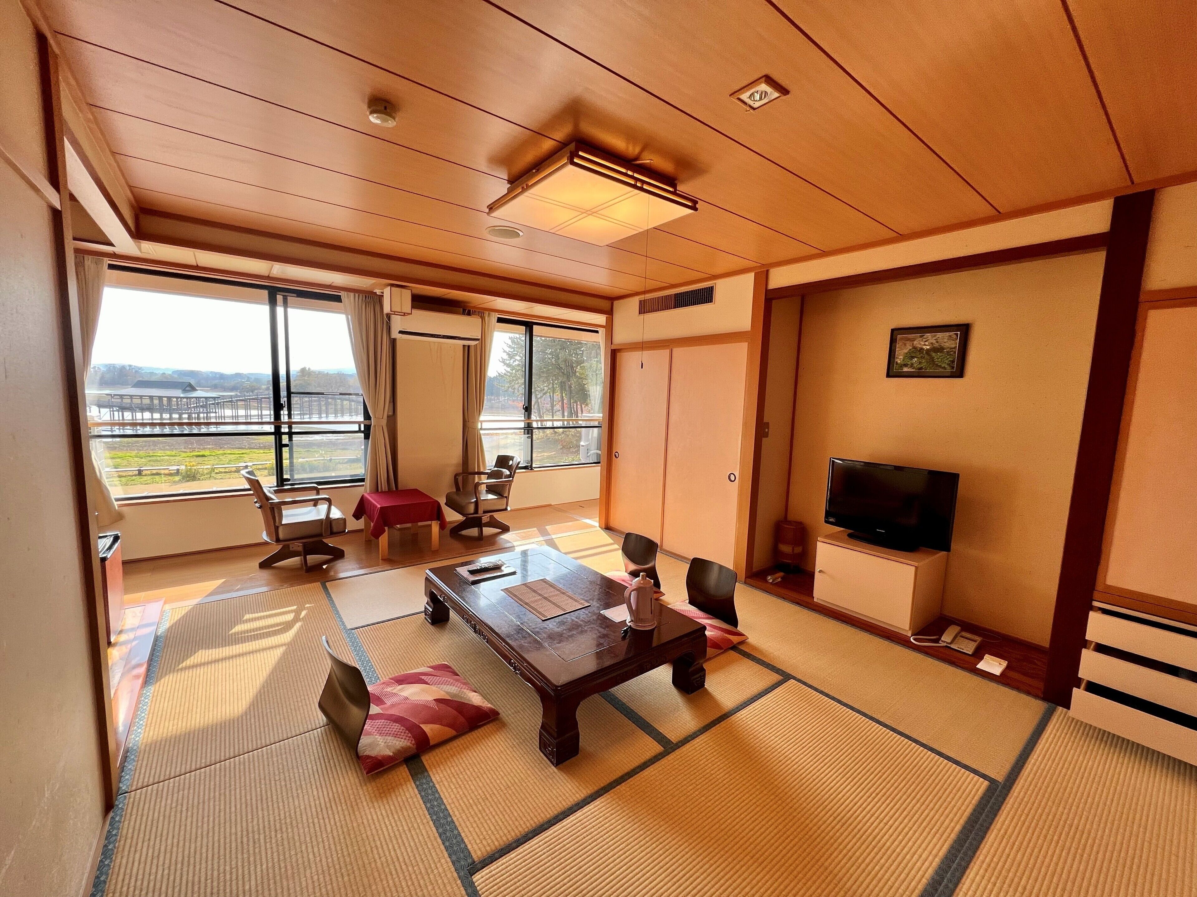 A traditional Japanese-style room with tatami flooring, a low table, chairs, a television, and a sliding door leading to a balcony.