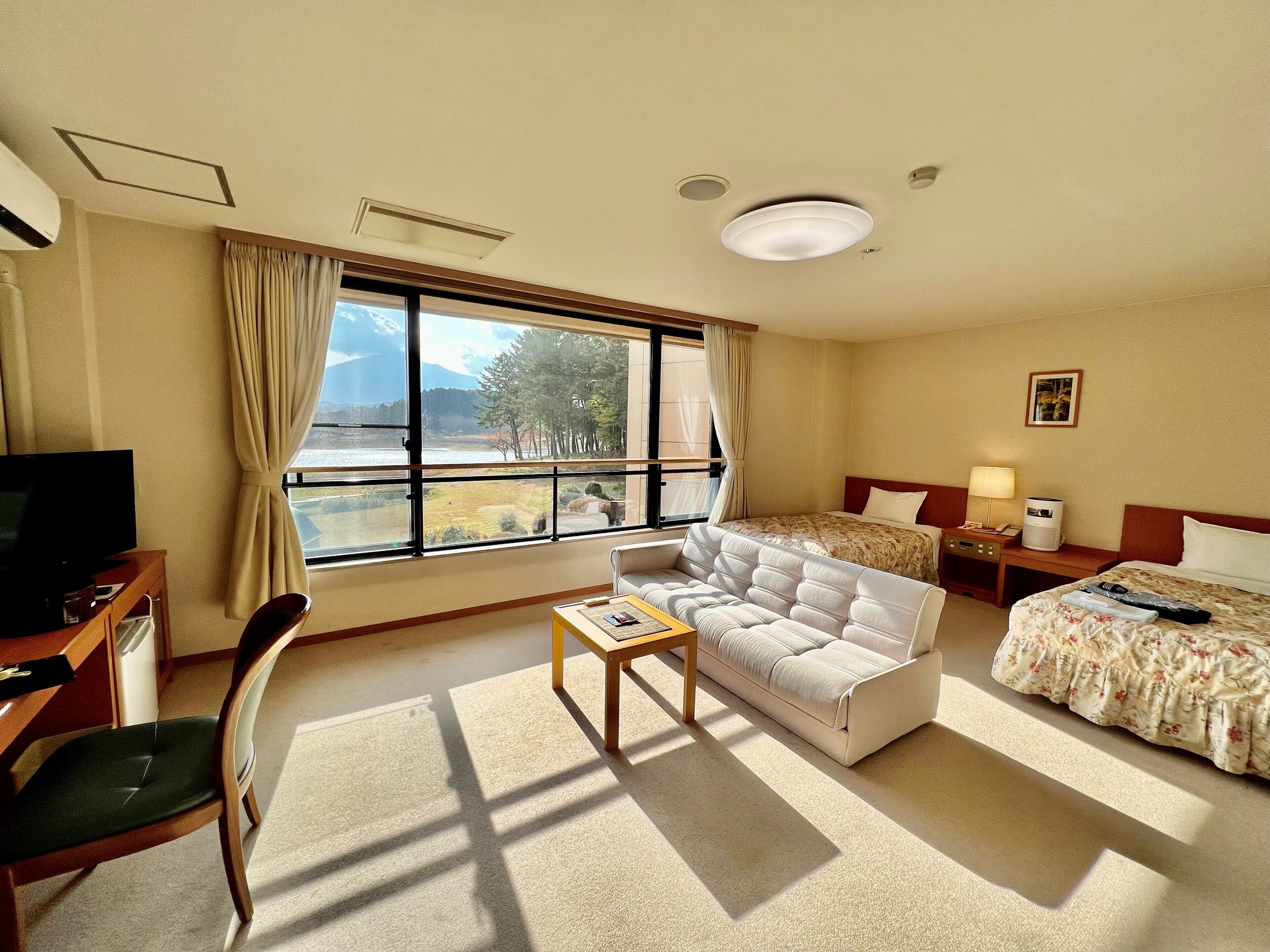 Una habitació d'hotel amb llit, sofà, televisió, escriptori i finestra amb vista a arbres i muntanyes.
