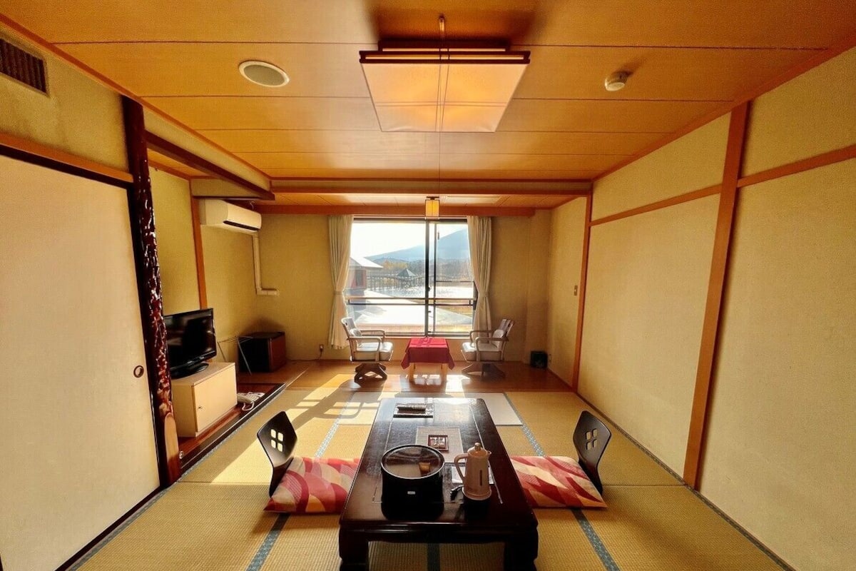 A traditional Japanese room with tatami flooring, a low table, and a TV on a cabinet.