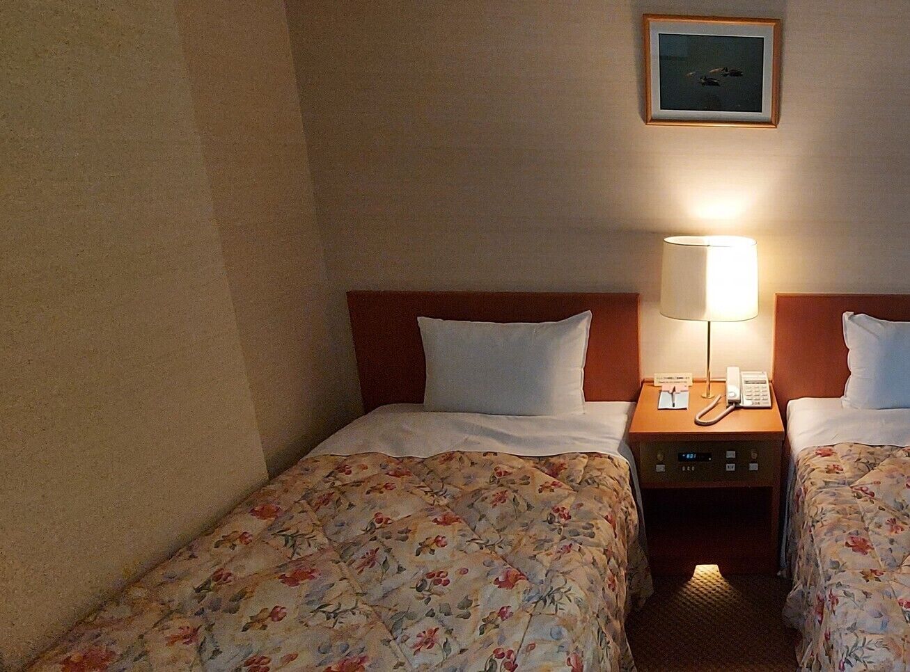 Habitació d'hotel amb dos llits, una taula de nit amb làmpada i telèfon, i un quadre al mur.