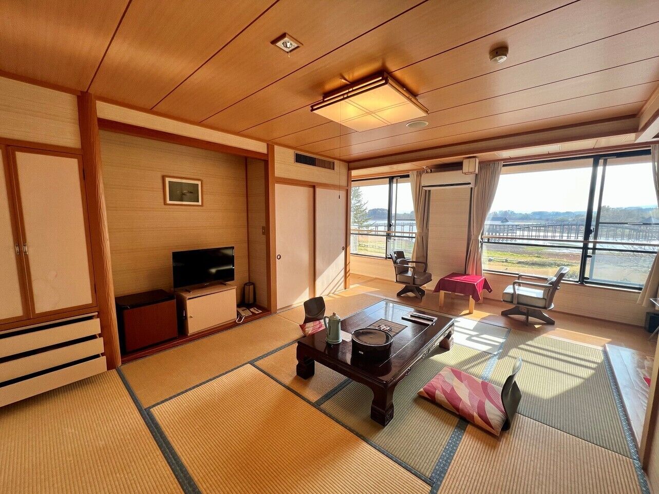 Habitació japonesa tradicional amb sòl de tatami, televisió, taula amb brossa i vista exterior.