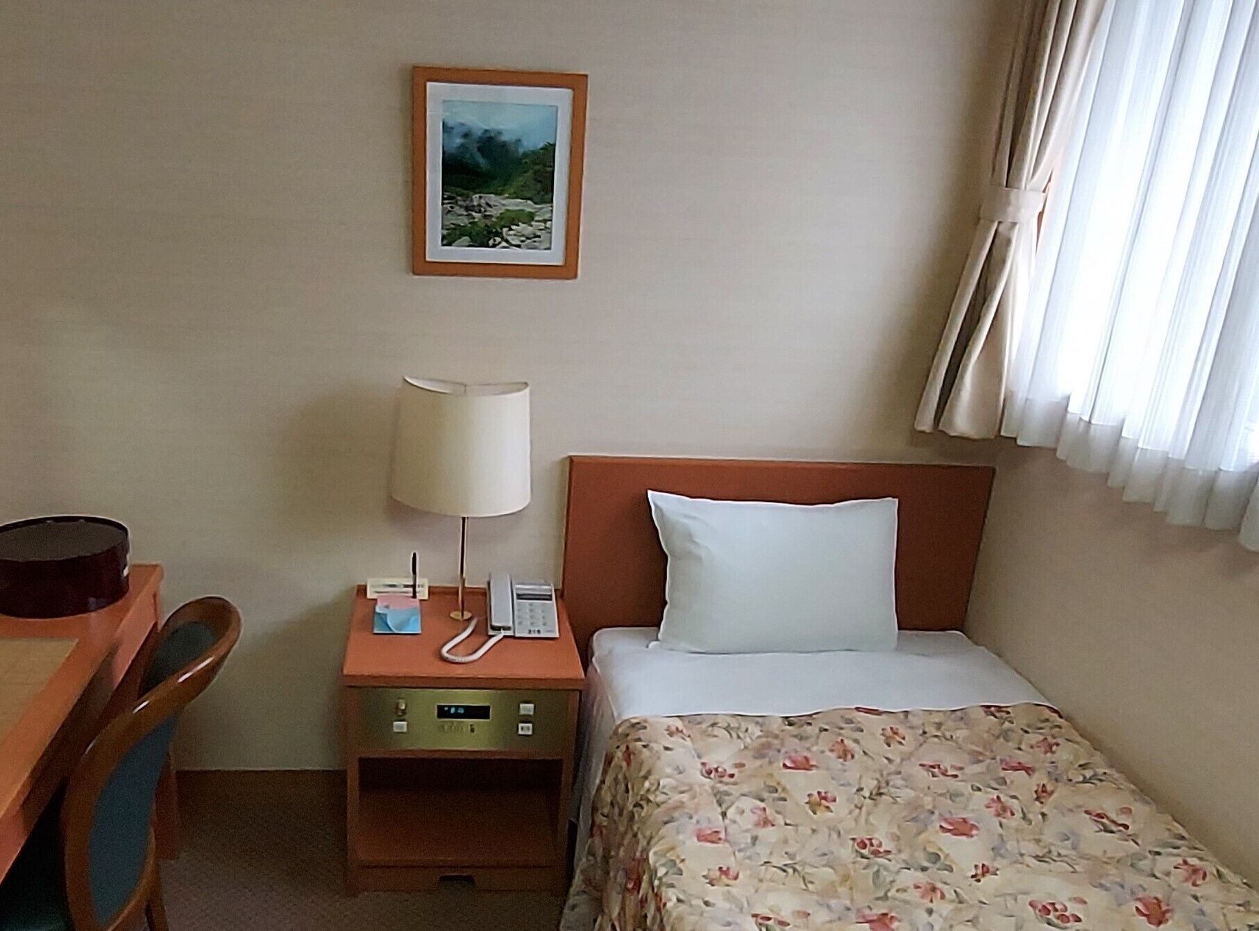 Una habitació d'hotel amb un llit, una taula de nit, un telèfon i un quadre a la paret.
