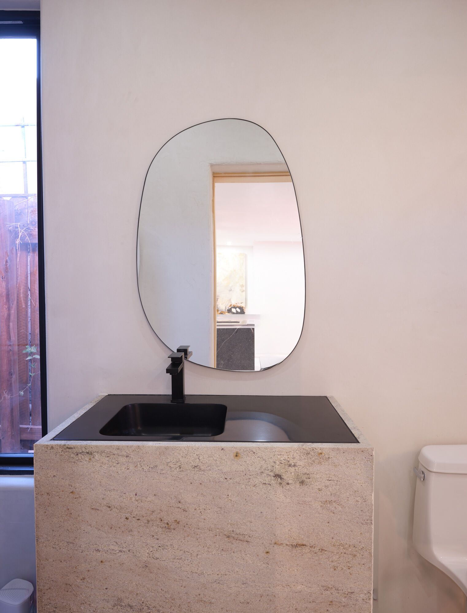 Un baño con lavamanos de granito, grifo negro y un espejo ovalado grande.