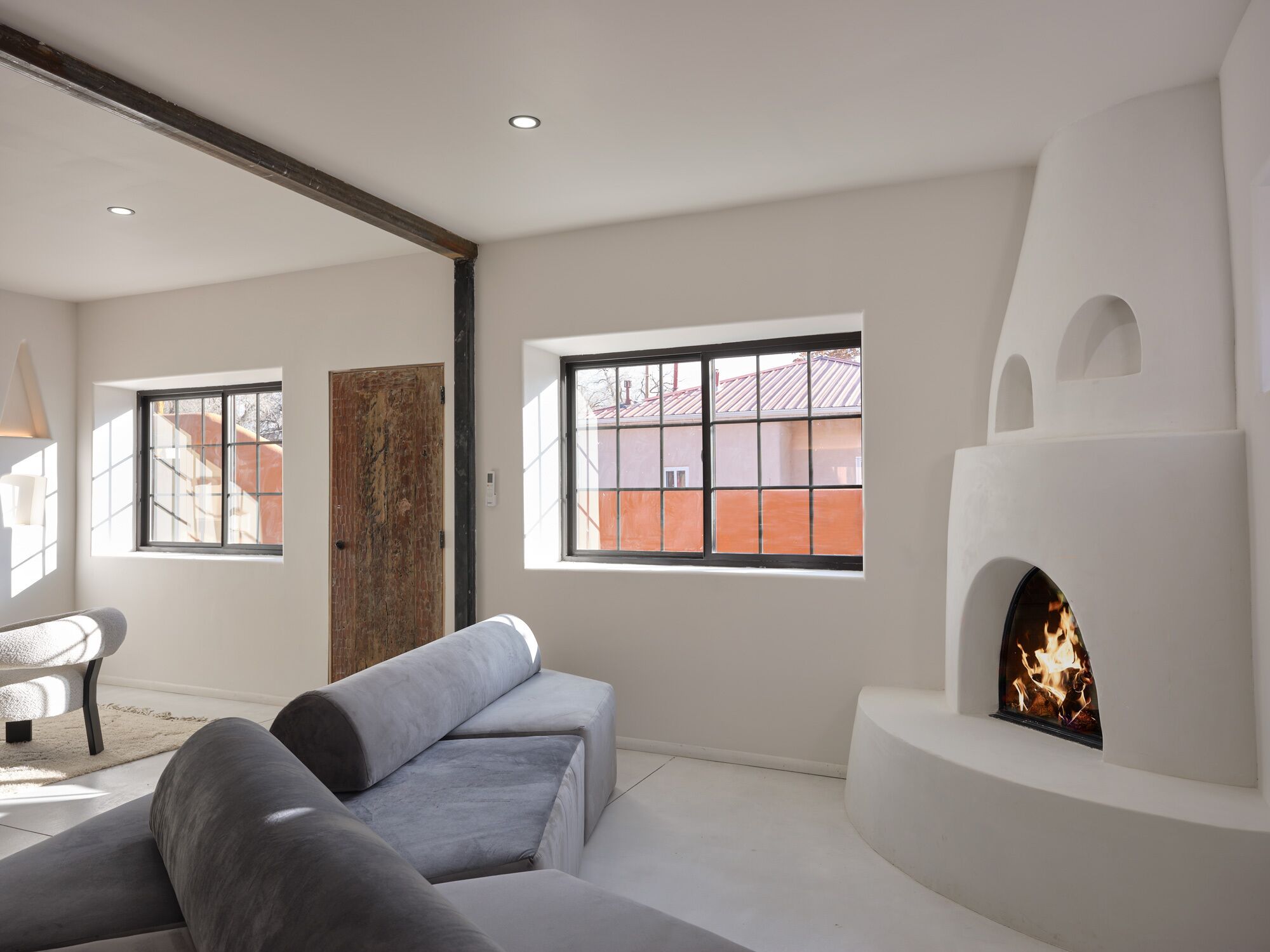 A modern living room with a fireplace, a sofa, and a large window with a view of buildings outside.