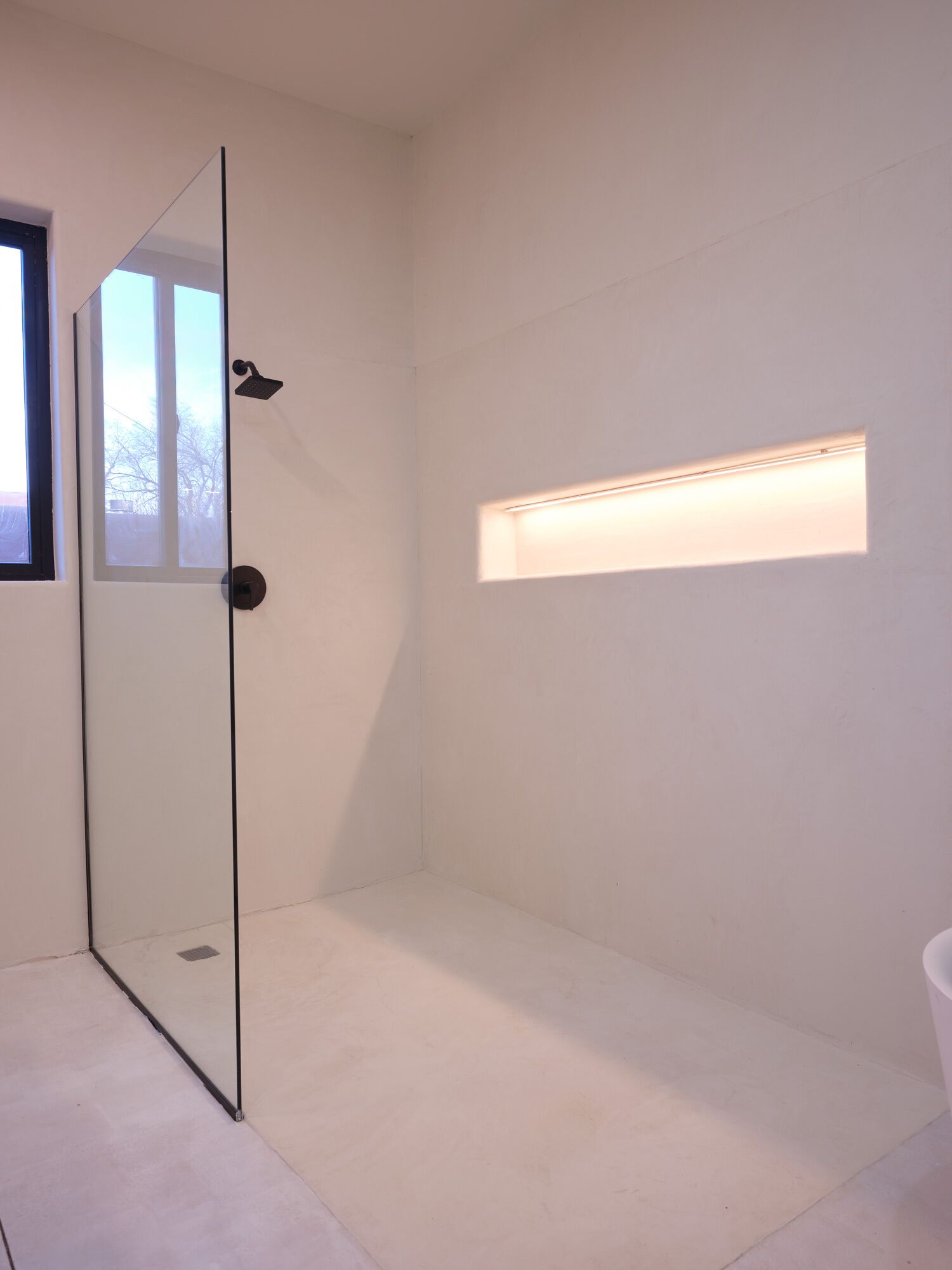 A modern bathroom with a glass shower door, a small window, and a built-in light fixture.