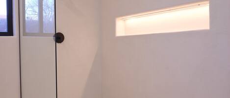 A modern bathroom with a glass shower door, a small window, and a built-in light fixture.