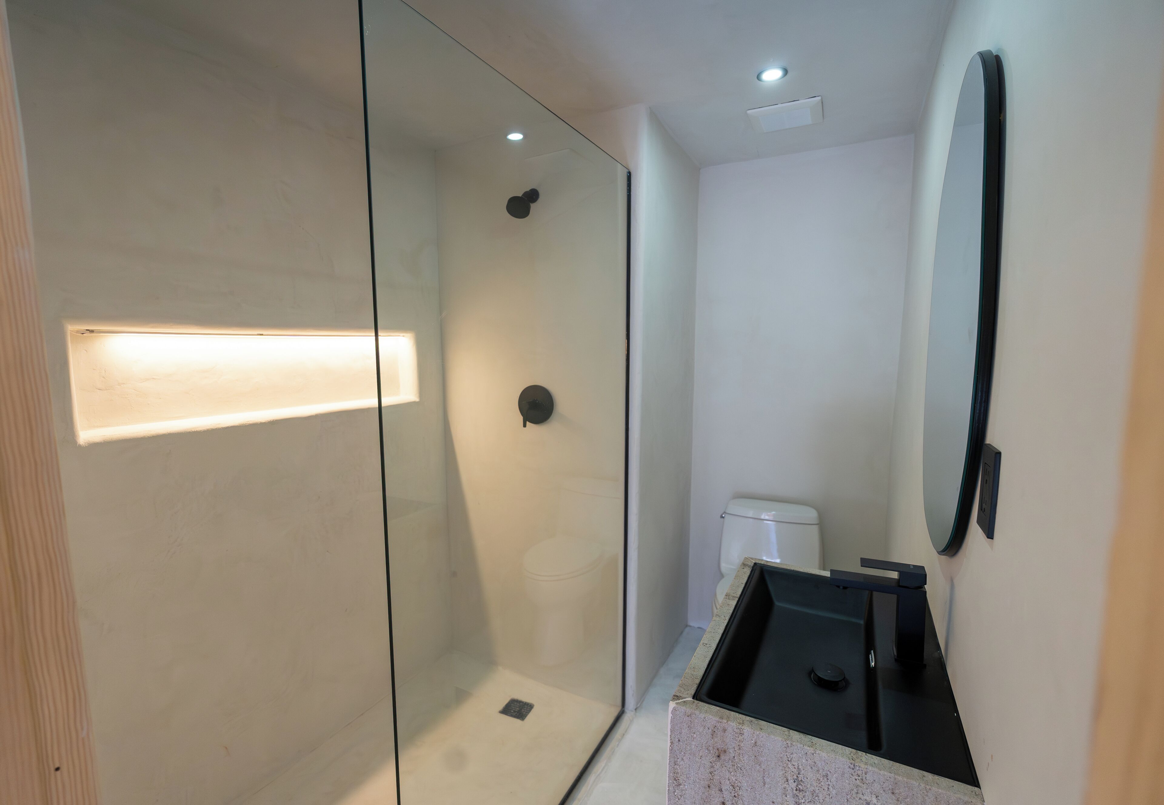 Un baño moderno con ducha de vidrio, inodoro y lavamanos con espejo.