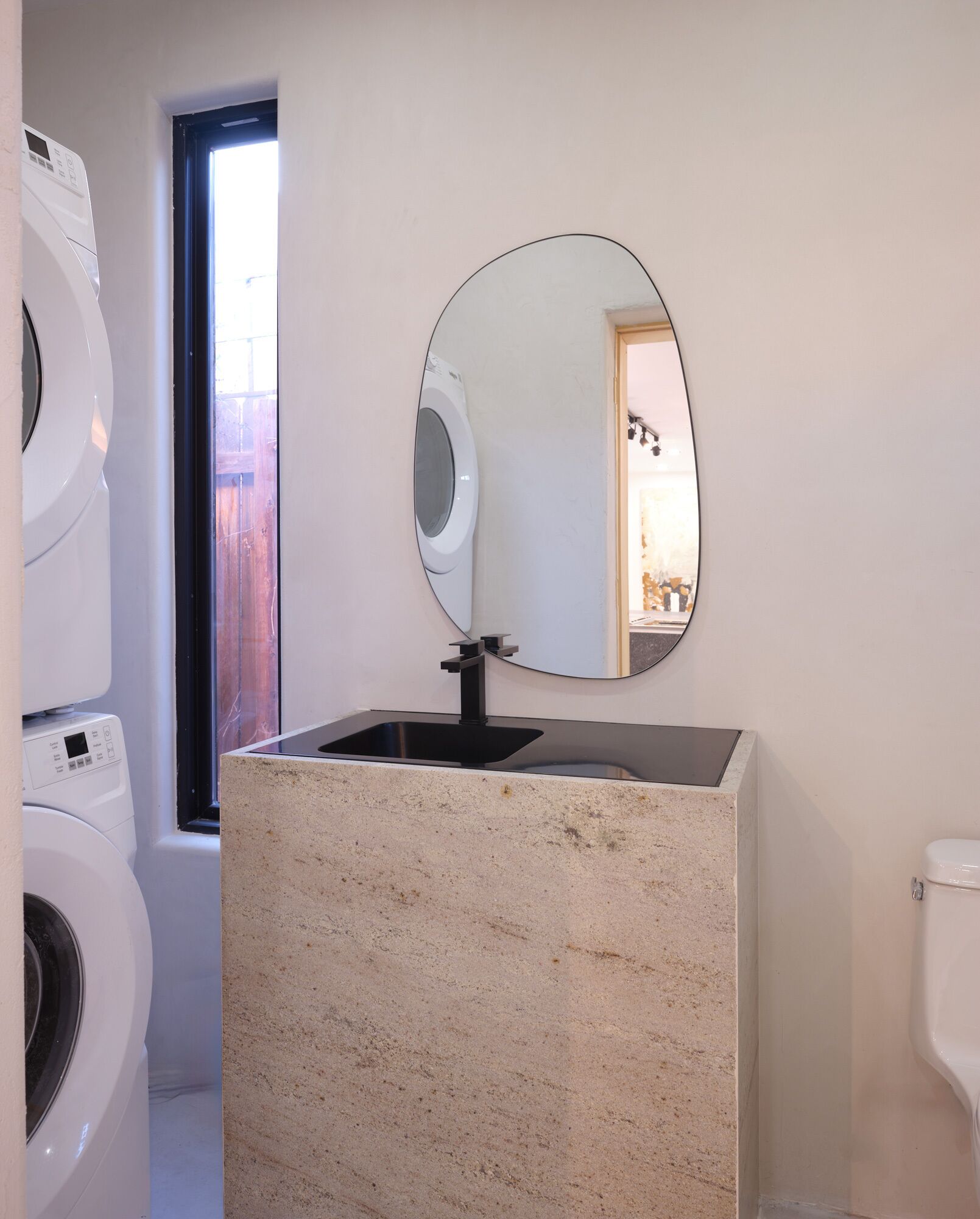 A bathroom with a freestanding washing machine, a sink with a large mirror, and a toilet.
