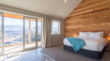 A bedroom with a large bed, wooden panel walls, and a view of a snowy landscape through large windows.