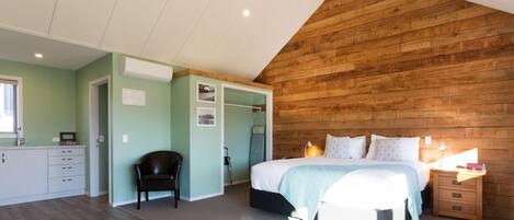 A bedroom with a wooden ceiling, a bed with pillows, a nightstand, and a chair.