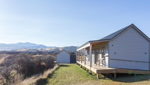 A single-story house with a covered porch, a small deck, and a view of mountains in the background. - Shotover Country Cottages (Lower Shotover)