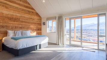 A bedroom with a large bed, a wooden wall, and a view of mountains through large windows.