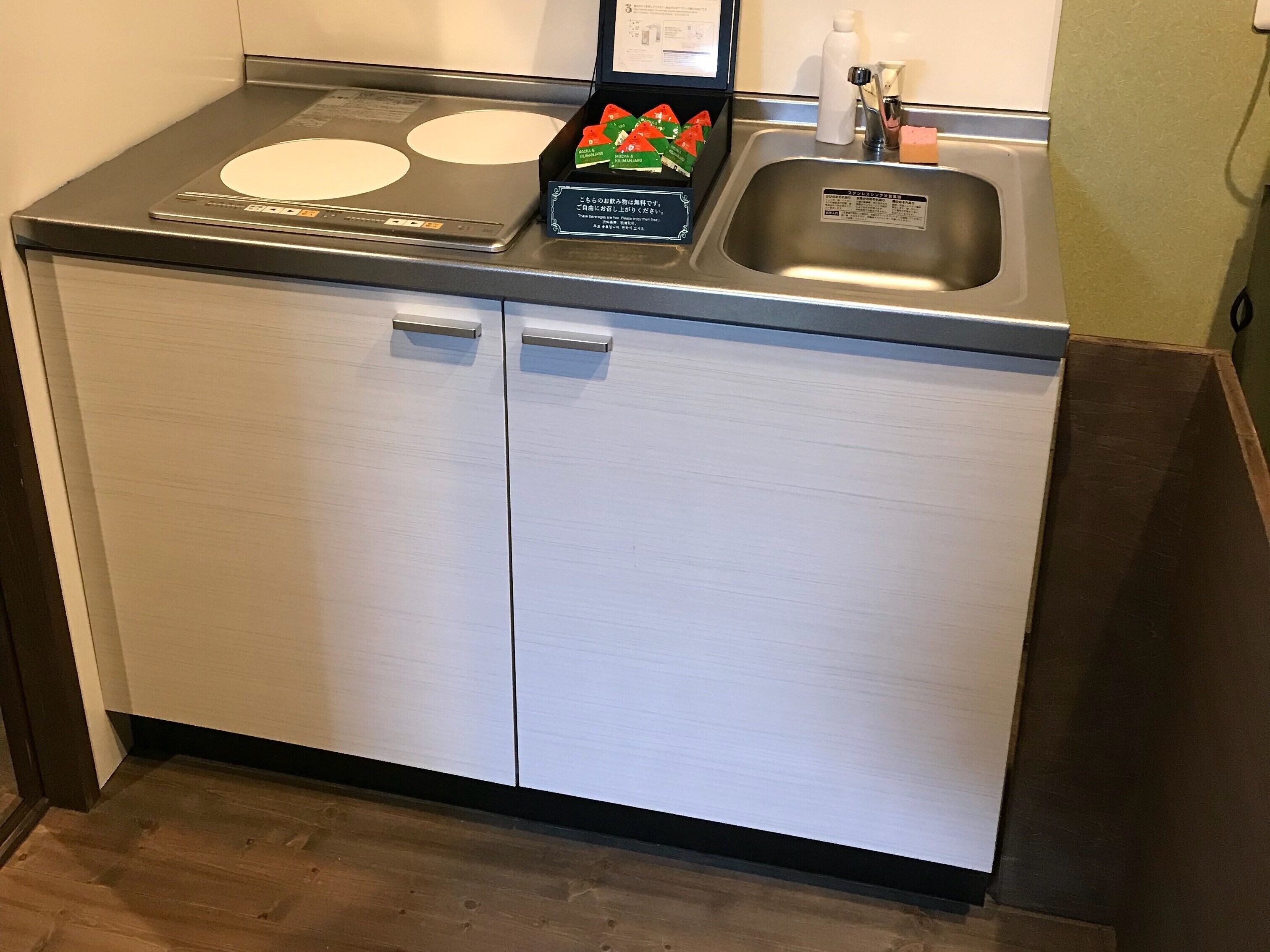 A kitchen with a stainless steel countertop, a sink, and two white cabinets.