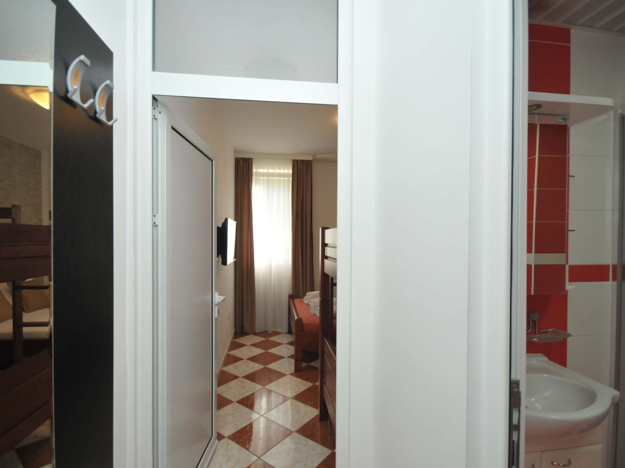 A hotel room with a checkered floor, a bed, a desk, and a bathroom with a red accent wall.
