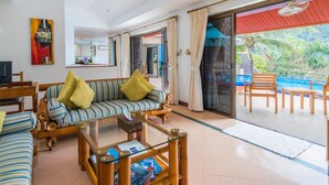 Ein geräumiger Wohnbereich mit einer Couch, einem Couchtisch und Blick auf einen Pool und Grünflächen.