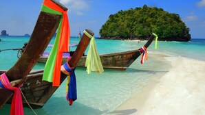 Ein Strand mit an Land gebundenen Holzbooten, klares türkisblaues Wasser und eine kleine Insel im Hintergrund.