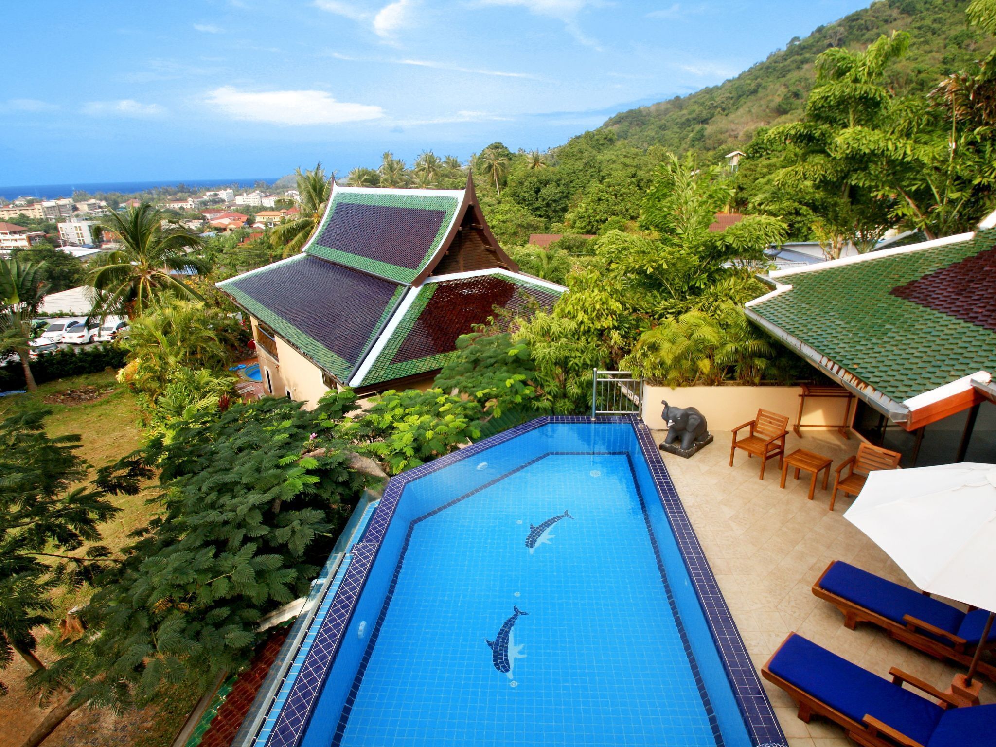 A swimming pool with dolphin tiles, surrounded by lush greenery and a view of a coastal town.