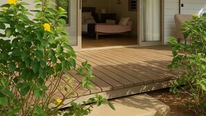A modern house with a wooden deck, a sliding glass door leading to a bedroom, and a garden with yellow flowers. - Fare Manini (Rimatara Island)