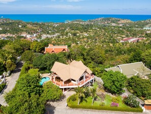 An aerial view of a residential area with a prominent house featuring a large swimming pool, surrounded by lush greenery and a clear view of the ocean. - Viewpoint Residence 4-Schlafzimmer-Villa Koh Samui by Interhome (Koh Samui)