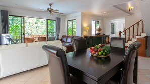 Amplia sala de estar con mesa de comedor, asientos cómodos, un balcón con vista a zonas verdes y una escalera que sube a otro nivel.