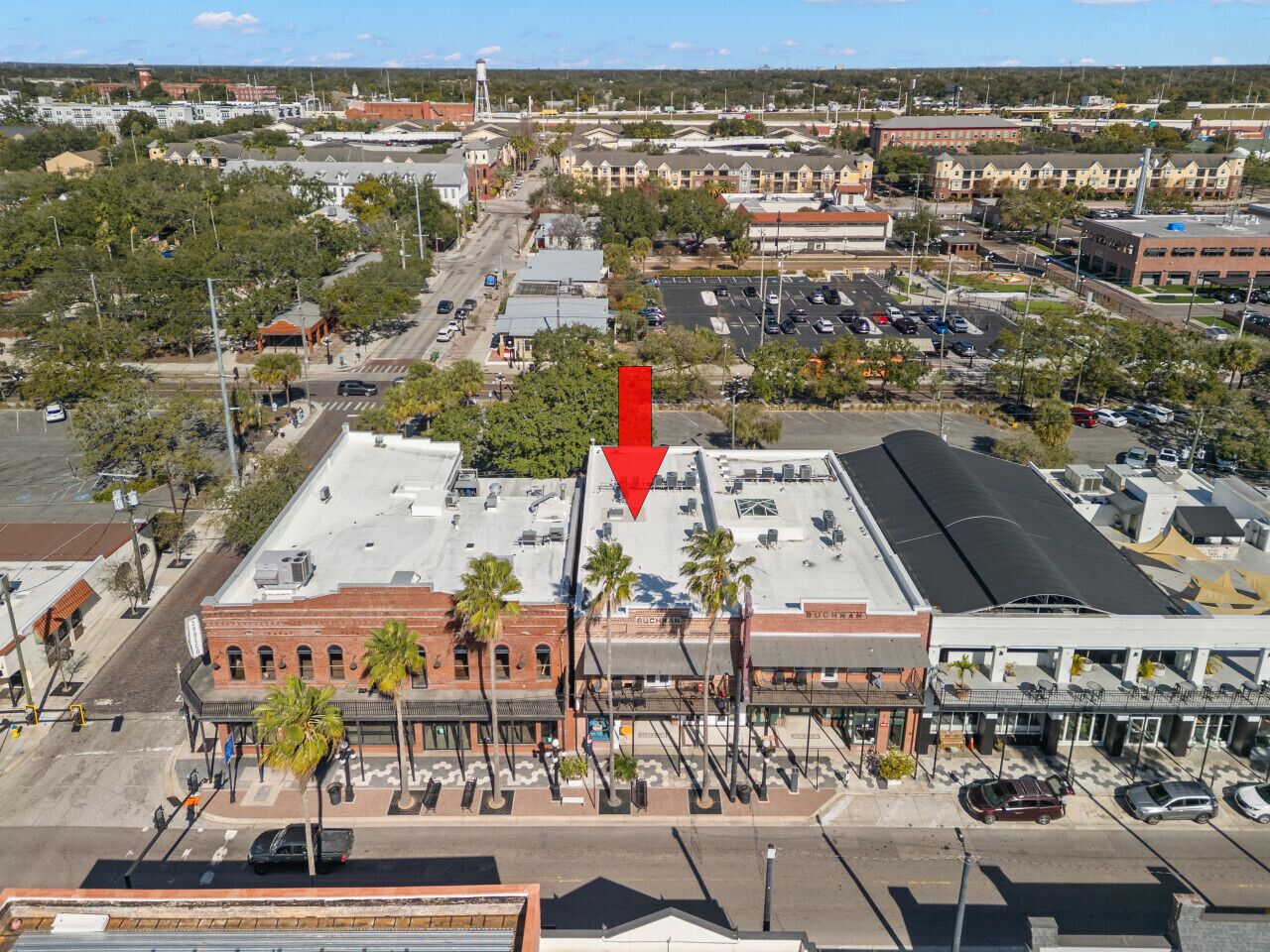An aerial view of a commercial area with a prominent building featuring a flat roof and a large red arrow pointing to it.