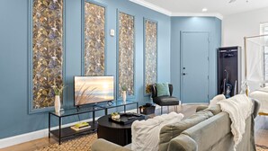 Una sala de estar con una pared azul, un televisor de pantalla plana, un sofá, una mesa de centro y un jarrón decorativo.