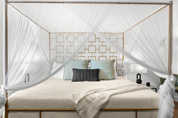 Una cama con dosel y cuatro columnas, un patrón geométrico en la pared, mesitas de noche y una lámpara de noche.