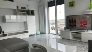 A modern living room with a grey sofa, a white coffee table, and a flat-screen TV on a white stand. There is a large window with a view of buildings outside. - Luxus-Residenz Westpark 2 by Interhome (Bucuresti)