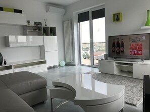 A modern living room with a grey sofa, a white coffee table, and a flat-screen TV on a white stand. There is a large window with a view of buildings outside. - Luxus-Residenz Westpark 2 by Interhome (Bucuresti)
