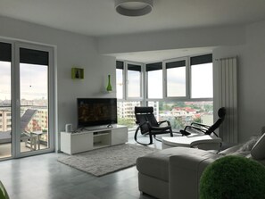A modern living room with a flat-screen TV, a sofa, a coffee table, and a chair. There is a large window with a view of buildings outside. - Luxus-Residenz Westpark 2 by Interhome (Bucuresti)