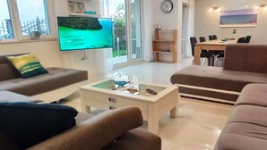 En moderne stue med et fladskærms-tv, sofaer, et sofabord og et spiseområde med stole.