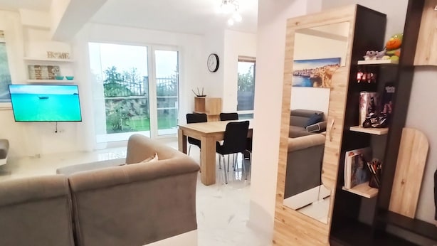 En moderne stue med sofa, tv, spiseplads med stole og en træbogreol.