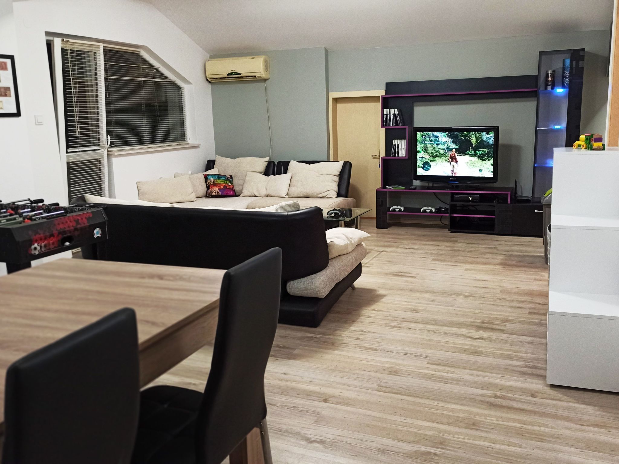 A modern living room with a sofa, a coffee table, a TV, and a foosball table.