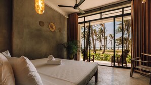 A bedroom with a large bed, a ceiling fan, a view of the beach, and a balcony with chairs. - Surfescape Sri Lanka (Ahangama)