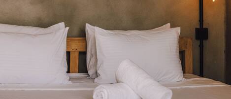 A bed with white linens, a wooden headboard, and a wall-mounted mirror with a sunburst design.