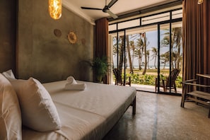 Ein Schlafzimmer mit einem großen Bett, einem Deckenventilator, Blick auf den Strand und einem Balkon mit Sitzgelegenheiten.