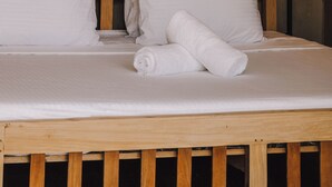 A bed with white linens, a wooden headboard, and a wall-mounted mirror with a sunburst design. - Surfescape Sri Lanka (Ahangama)