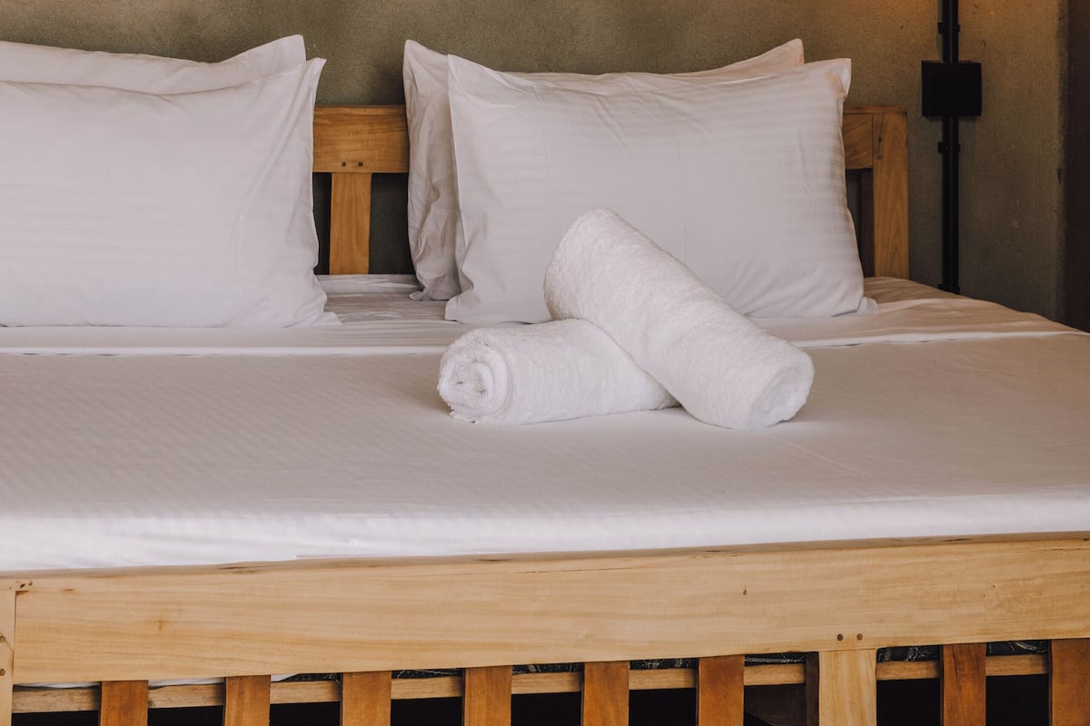 A bed with white linens, a wooden headboard, and a wall-mounted mirror with a sunburst design.