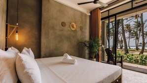 A bedroom with a large bed, a ceiling fan, a wall-mounted light, and a view of the beach. - Surfescape Sri Lanka (Ahangama)