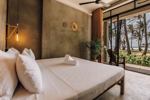 A bedroom with a large bed, a ceiling fan, a wall-mounted light, and a view of the beach. - Surfescape Sri Lanka (Ahangama)