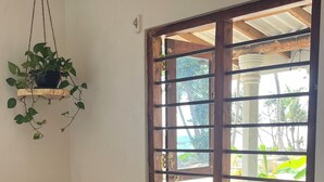 A room with a wooden desk, a chair, a hanging plant, and a window with a view of greenery. - Surfescape Sri Lanka (Ahangama)
