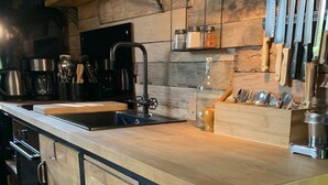 Une cuisine moderne avec un plan de travail en bois, un évier et une cuisinière encastrée. Des étagères au-dessus du plan de travail servent à ranger des bocaux et des ustensiles.