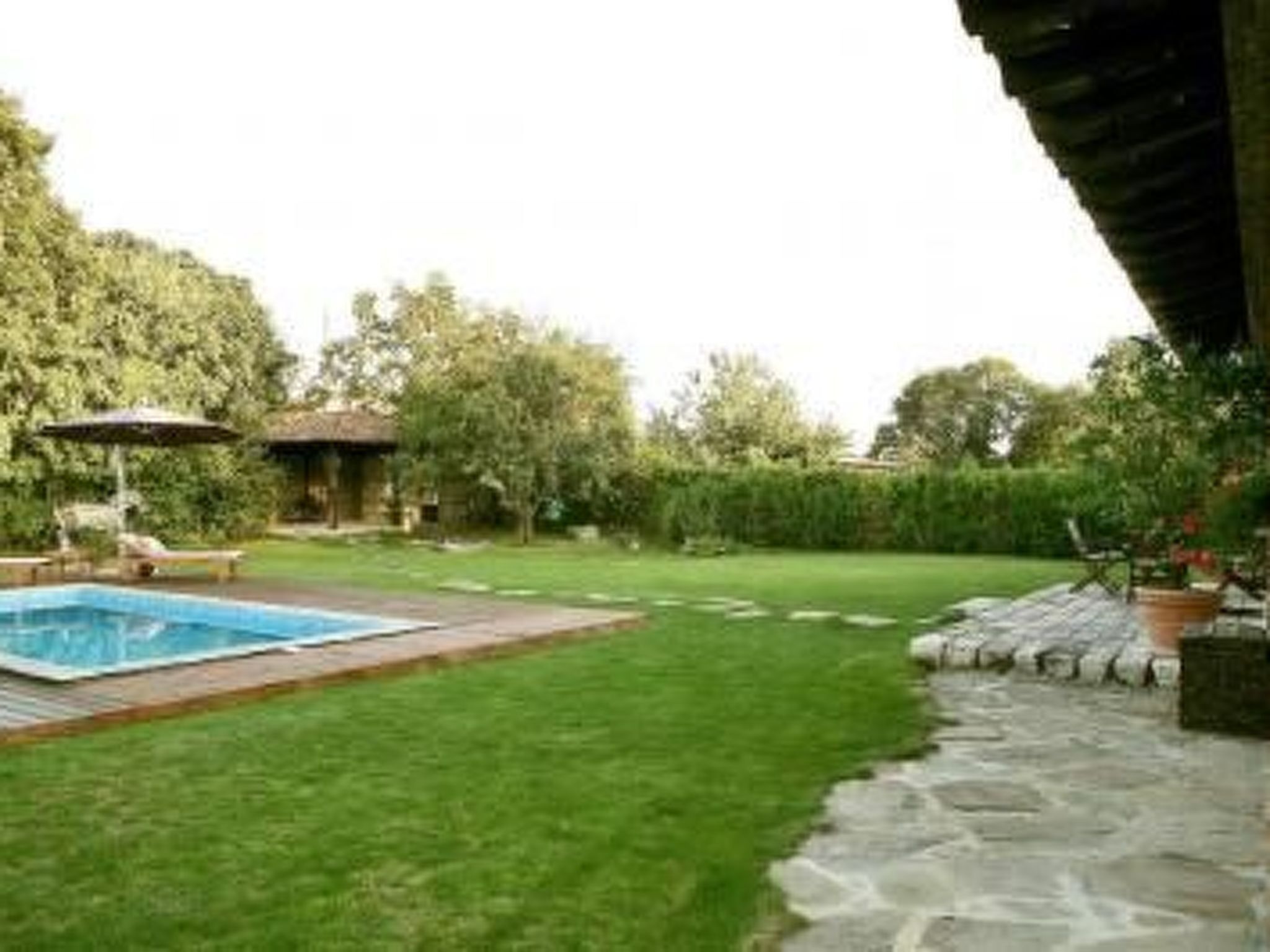 A backyard with a swimming pool, a patio area, and a stone pathway.