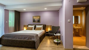 Une chambre d’hôtel moderne avec un grand lit, une table de chevet avec une lampe, un fauteuil à rayures et une petite table d’appoint avec une plante.