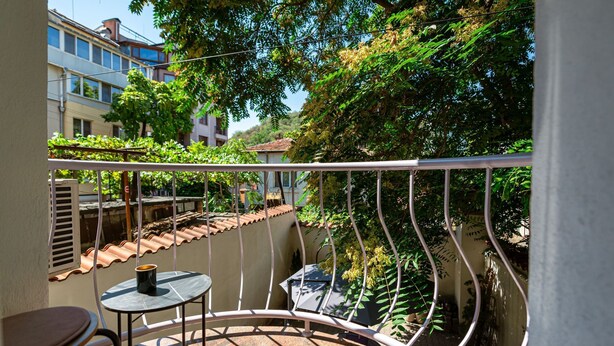 Un balcon avec une table ronde et des chaises, une vue sur des immeubles et un arbre aux feuilles vertes.
